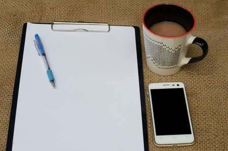 The note book and paper writing set with smart phone and a cup of coffee ,on sackcloth backgroundの写真素材