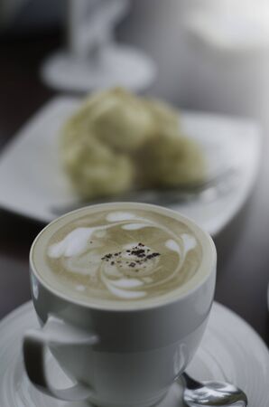 top view and soft focus on foam of  cappuccino in a white cup with a spoon and blur dessert backgroundの写真素材