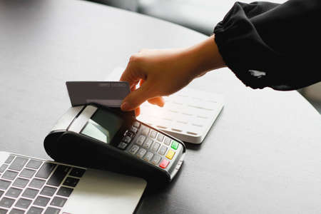 A woman using hand credit card swipe machine for sell products in the shop. Concept of spending via credit card.の写真素材