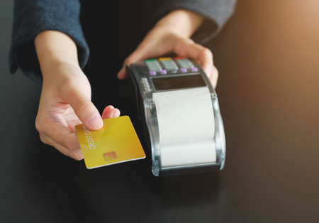 A woman using hand credit card swipe machine for sell products in the shop. Concept of spending via credit card.の写真素材