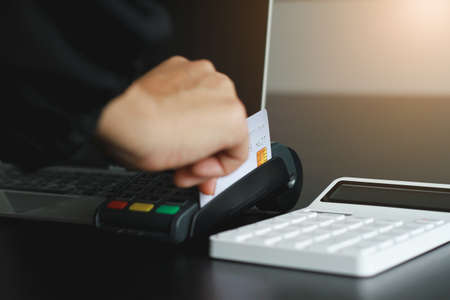 A woman using hand credit card swipe machine for sell products in the shop. Concept of spending via credit card.の写真素材
