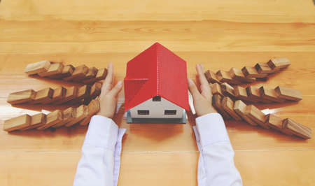 Woman hand stopping risk the wooden blocks from falling on house, Home insurance and security concept.の写真素材