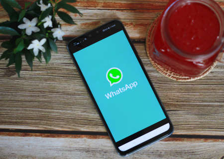 CHIANG MAI, THAILAND - August 11, 2020 : Whatsapp logo on Smartphone with whatsapp app on the screen on desk office. Top view of coffee shop.のeditorial素材