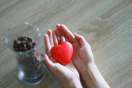 Woman holding a red heart on palm with wood grain background Donation ideaの写真素材
