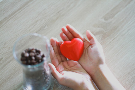 Woman holding a red heart on palm with wood grain background Donation ideaの写真素材