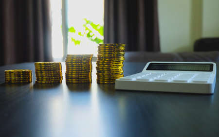 Stack of golden coins and calculator on table with earning profit concept. Gold coins or currency of business.の写真素材