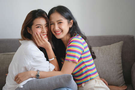 lgbtq, lgbt concept, homosexuality, two beautiful women in love happily playing tablet in a cozy homeの写真素材