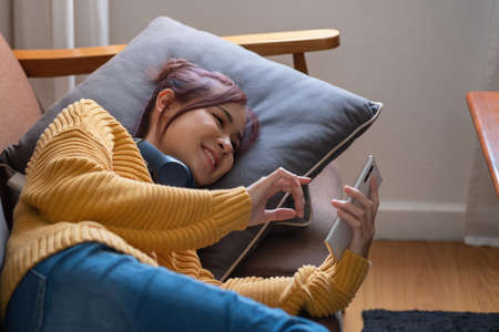 relax, de-stress, holiday, happy, Asian woman relaxing at home listening to music from smartphone and laptop happily.の写真素材