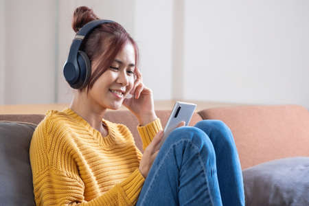 relax, de-stress, holiday, happy, Asian woman relaxing at home listening to music from smartphone and laptop happily.の写真素材