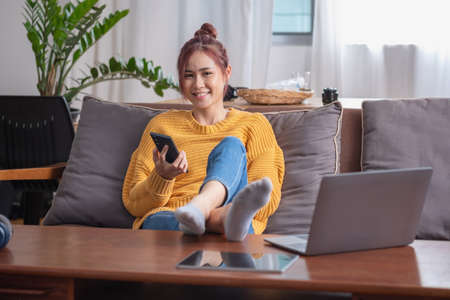 relax, de-stress, holiday, happy, Asian woman relaxing at home listening to music from smartphone and laptop happily.の写真素材
