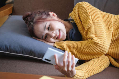 relax, de-stress, holiday, happy, Asian woman relaxing at home listening to music from smartphone and laptop happily.の写真素材