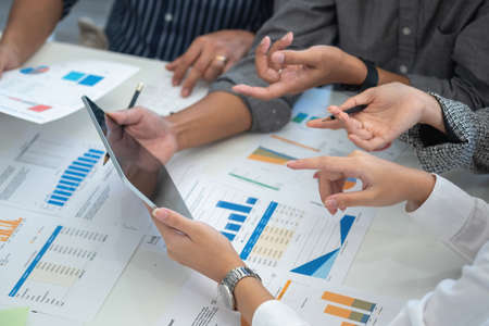 Team of business use calculators and graph analysis computer laptop tablets to plan marketing...