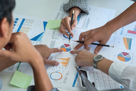 A team of businessmen plan with their laptops and graph charts for their profits and use a calculator to calculate their company's annual balance.の写真素材