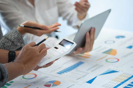 Team of business use calculators and graph analysis computer laptop tablets to plan marketing...