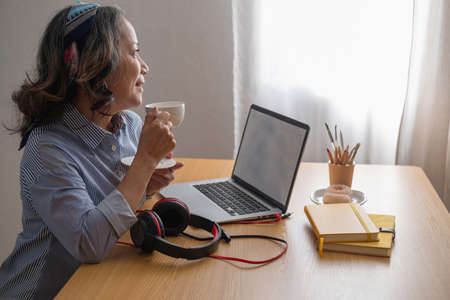relax time, Portrait of an older woman sitting on her laptop listening to music and having a drink...