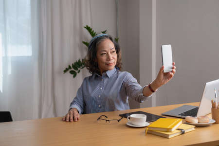Portrait of an elderly woman holding a cell phone to take a picture of herself for future reference.
