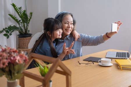 Portrait of an elderly woman holding a cell phone to take a picture of herself and her granddaughter...