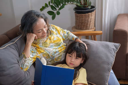 Portrait of an elderly woman and granddaughter reading a book to enhance reading skills and family...
