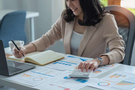 Portrait of a female accountant using a calculator and laptop to calculate balance using graphs for...