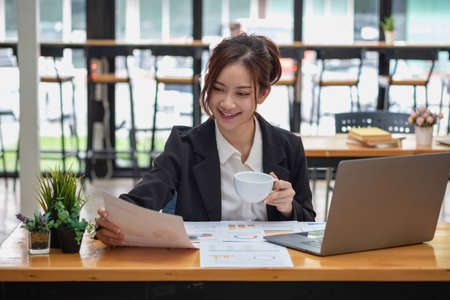 Marketing, Financial, Accounting, Planning, Business women analyze company results and profits with graph statistics. Use a laptop computer and a calculator to calculate the company's balance.の写真素材