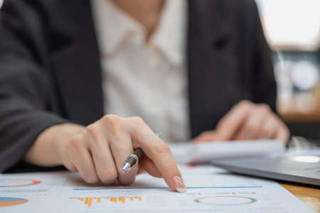 Marketing, Financial, Accounting, Planning, Business women analyze company results and profits with graph statistics. Use a laptop computer and a calculator to calculate the company's balance.の写真素材