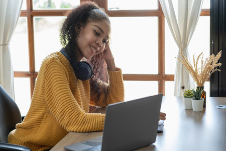 African woman, American, using laptop computer and wearing headphones for online learning.