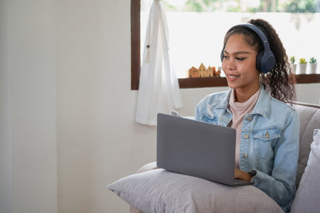 An African American woman uses a laptop, smartphone, tablet and music headset in her home to relax.の写真素材