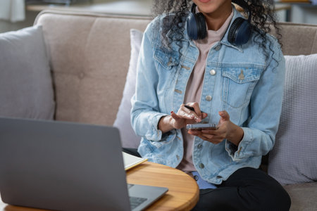 An African American woman uses a smartphone and puts on a music headset in her home to relax.の写真素材