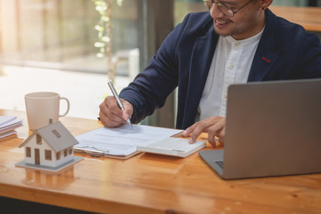 Accountant, businessman, real estate agent, businessman handing model house to customers along with house interest calculation documents for customers to sign.の写真素材