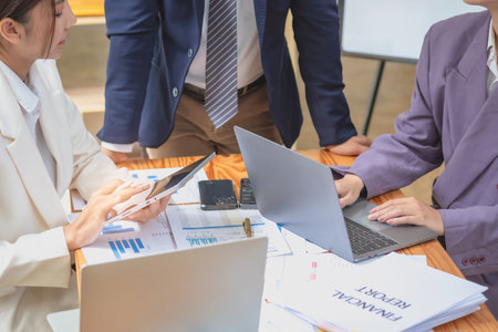 Asian business team consists of marketing staff. accountant and financial officer Help each other analyze company profits using tablets. calculator Laptop computers, graph paper, and corporate pens.の写真素材