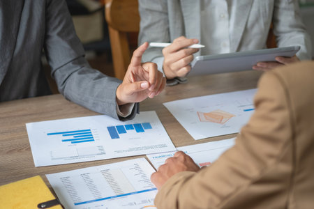 A team of businessmen plan with their laptops and graph charts for their profits and use a calculator to calculate their company is annual balance.の写真素材