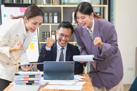 Team business three smiling and happy Asian men and women team using tablets and laptops brainstorm and plot statistics on a corporate chart board inside the company. Colleagues concept.の写真素材