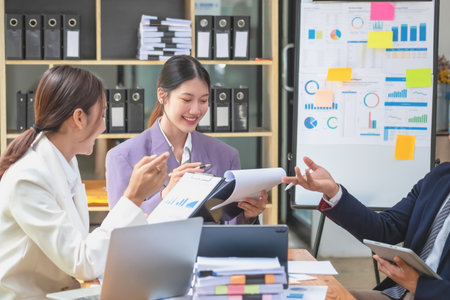 Asian business team consists of marketing staff. accountant and financial officer Help each other analyze company profits using tablets. calculator Laptop computers, graph paper, and corporate pens.の写真素材