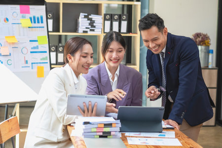 A team of businessmen plan with their laptops and graph charts for their profits and use a calculator to calculate their company's annual balance.の写真素材