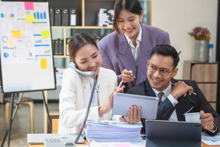 Team business three smiling and happy Asian men and women team using tablets and laptops brainstorm and plot statistics on a corporate chart board inside the company. Colleagues concept.