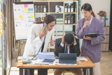 A team of three Asian businessmen is working inside an office where businessmen in black suits are being ordered by their supervisors and bosses a lot causing stress at work. burnout conceptの写真素材