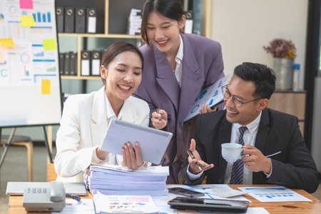 Asian business team consists of marketing staff. accountant and financial officer Help each other analyze company profits using tablets. calculator Laptop computers, graph paper, and corporate pens.の写真素材