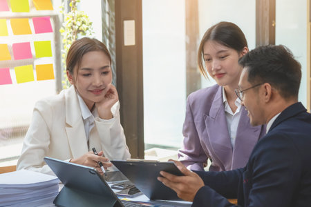Asian business team consists of marketing staff. accountant and financial officer Help each other analyze company profits using tablets. calculator Laptop computers, graph paper, and corporate pens.の写真素材