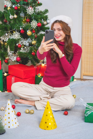Merry Christmas and Happy Holidays! Young woman with a beautiful face in a red shirt shows joy with gift boxes in a house with a Christmas tree decorated with Christmas tree.  Portrait before Xmasの写真素材