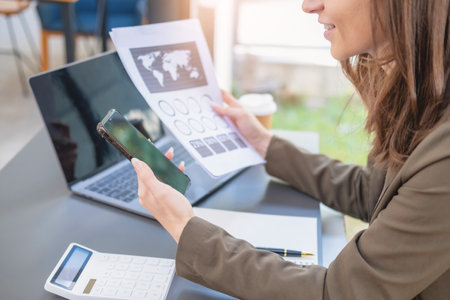 Marketing, Finance, Accounting, Planning, Businesswoman of bi nationality is talking with a customer representing a company distributor using a smartphone with laptop pen and notepad on office desk.の写真素材