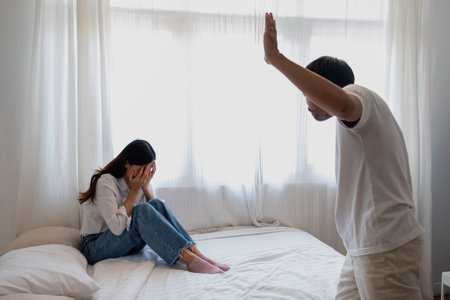 Internal violence. family conflict Men attack and beat women at home. Frightened woman covering her face sitting on the bed. She was scared.の写真素材