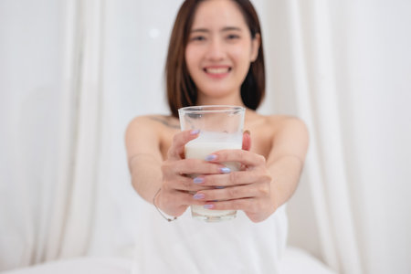 Portrait of young cheerful Asian woman drinking healthy milk on the morning of the holiday Good rest and healthy lifestyle concept.の写真素材