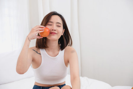 Portrait of white Asian woman with a tattoo sitting on the bed relaxing and playing laptop on weekend There was bread and fruit and red apples on a white bed to eat. holiday conceptの写真素材