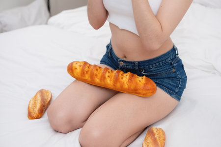 Close-up shot of a white Asian woman with a tattoo sitting on the bed holding bread and eating junk food. without taking care of one's health to cause obesity, obesity concept.の写真素材