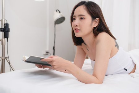 Portrait of white Asian woman with tattoo resting in bed to rest and relax inside white bedroom on her holiday, holiday morning concept.の写真素材