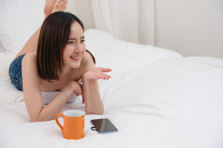 Portrait of white Asian woman with tattoo resting in bed to rest and relax inside white bedroom on her holiday, holiday morning concept.の写真素材