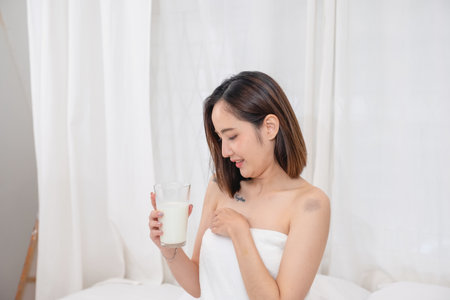 Portrait of young cheerful Asian woman drinking healthy milk on the morning of the holiday Good rest and healthy lifestyle concept.の写真素材