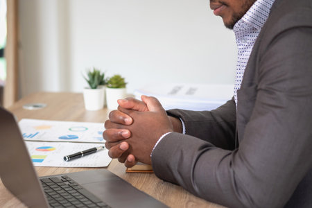 African American businessman analyzing laptop graph paperwork in office holding documents preparing portfolio analysis report Black male analyst doing paperwork in the workplace using the computer.の写真素材