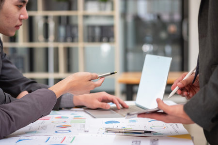 Asian business team consists of marketing staff. accountant and financial officer Help each other analyze company profits using tablets. calculator Laptop computers, graph paper, and corporate pens.の写真素材