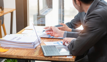 Asian business team consists of marketing staff. accountant and financial officer Help each other analyze company profits using tablets. calculator Laptop computers, graph paper, and corporate pens.の写真素材